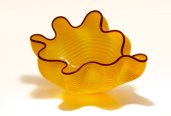 Two abstract blown-glass sculptures by Dale Chihuly in vivid saffron yellow, featuring organic, seaform-inspired shapes with contrasting lip wraps; one larger and one smaller form are displayed together, emphasizing scale, color saturation, and biomorphic movement characteristic of Chihuly's modern glass work.