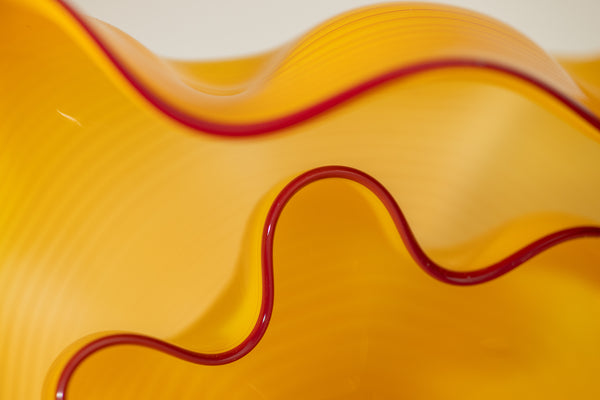 Two abstract blown-glass sculptures by Dale Chihuly in vivid saffron yellow, featuring organic, seaform-inspired shapes with contrasting lip wraps; one larger and one smaller form are displayed together, emphasizing scale, color saturation, and biomorphic movement characteristic of Chihuly's modern glass work.