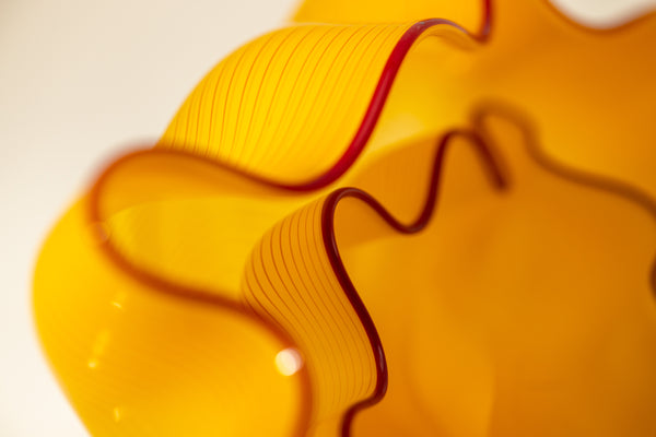 Two abstract blown-glass sculptures by Dale Chihuly in vivid saffron yellow, featuring organic, seaform-inspired shapes with contrasting lip wraps; one larger and one smaller form are displayed together, emphasizing scale, color saturation, and biomorphic movement characteristic of Chihuly's modern glass work.