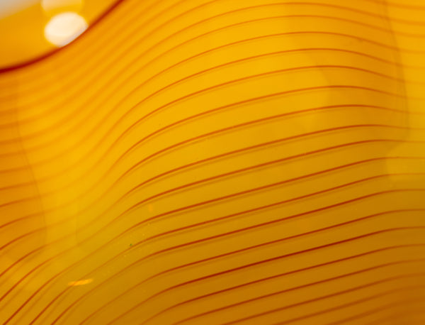 Two abstract blown-glass sculptures by Dale Chihuly in vivid saffron yellow, featuring organic, seaform-inspired shapes with contrasting lip wraps; one larger and one smaller form are displayed together, emphasizing scale, color saturation, and biomorphic movement characteristic of Chihuly's modern glass work.