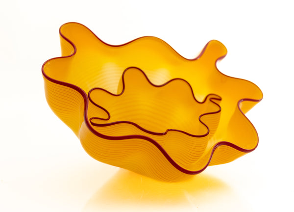 Two abstract blown-glass sculptures by Dale Chihuly in vivid saffron yellow, featuring organic, seaform-inspired shapes with contrasting lip wraps; one larger and one smaller form are displayed together, emphasizing scale, color saturation, and biomorphic movement characteristic of Chihuly's modern glass work.