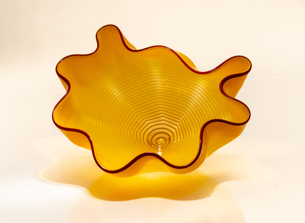 Two abstract blown-glass sculptures by Dale Chihuly in vivid saffron yellow, featuring organic, seaform-inspired shapes with contrasting lip wraps; one larger and one smaller form are displayed together, emphasizing scale, color saturation, and biomorphic movement characteristic of Chihuly's modern glass work.
